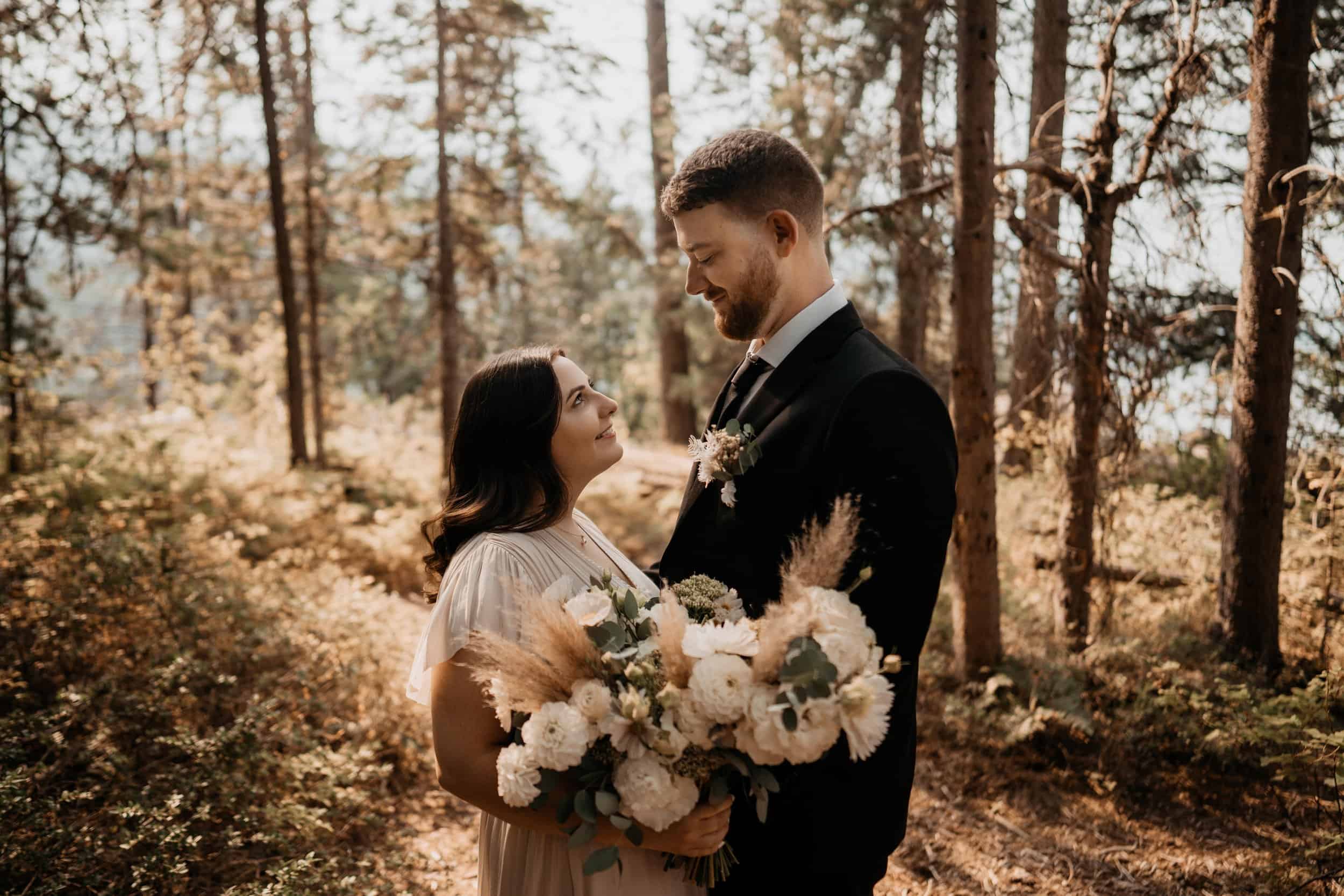 couple facing each other after eloping, taking sunset portraits in forest with bouquet