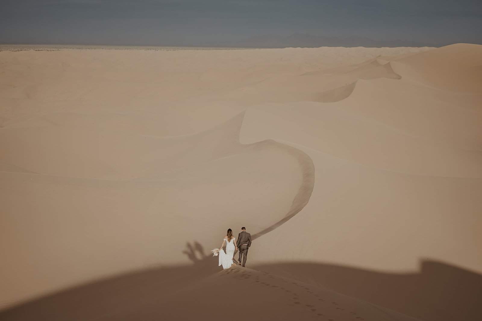 Bride and groom walking across sand dunes for Colorado elopement