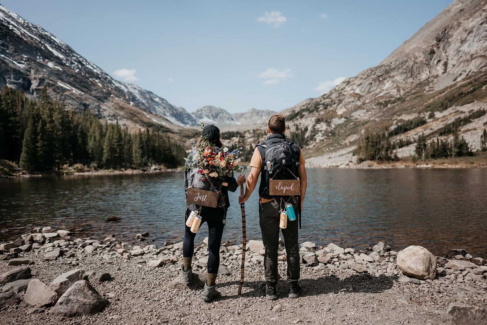 Bride and groom wearing hiking backpacks with signs that say "just eloped" after their elopement in Colorado