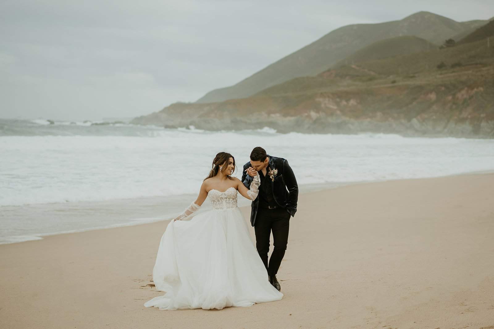Groom kissing bride's hand while walking along the beach during Hawaii elopement